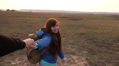 Genç çift el ele tutuşuyor. Sırt çantalı mutlu kadın adamı elinden tutar ve ona yol gösterir. Turistlerden oluşan bir takımda çalışmak. Aşık eller gün batımında seyahat eder..