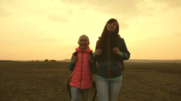 Mutter und Kind gehen zum Sonnenuntergang in die Berge. glückliche Familie auf Urlaubsreisen. Konzept des sportlichen Familientourismus. Mutter und Tochter reisen mit Rucksack gegen den Himmel. — Stockfoto