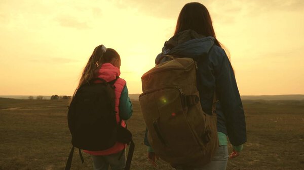 Mom and daughter travel with a backpack against the sky. tourists mother and child go to sunset in the mountains. happy family on vacation travels. sports tourism concept.