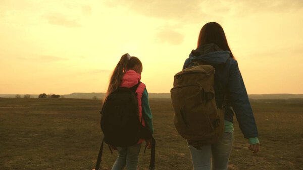 Mom and daughter travel with a backpack against the sky. tourists mother and child go to sunset in the mountains. happy family on vacation travels. sports tourism concept.