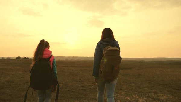 Mom and daughter travel with a backpack against the sky. tourists mother and child go to sunset in the mountains. happy family on vacation travels. sports tourism concept.