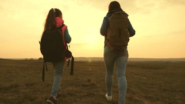 Mom and daughter travel with a backpack against the sky. tourists mother and child go to sunset in the mountains. happy family on vacation travels. sports tourism concept.