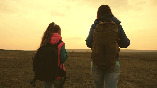 Mom and daughter travel with a backpack against the sky. tourists mother and child go to sunset in the mountains. happy family on vacation travels. sports tourism concept.