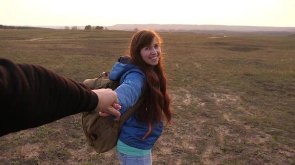 Jong stel houdt elkaars hand vast. gelukkige vrouw met rugzak houdt man bij de hand en leidt hem. werken in een team van toeristen. handen in de liefde zijn reizen bij zonsondergang. — Stockfoto