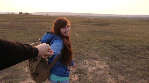 Ein junges Paar, das Händchen hält, ist unterwegs. Eine glückliche Frau mit Rucksack hält den Mann an der Hand und führt ihn. Arbeit in einem Team von Touristen. Verliebte Hände sind bei Sonnenuntergang unterwegs. — Stockfoto