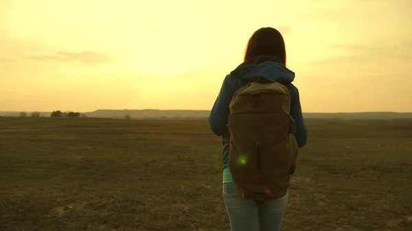 Mädchen, das mit einem Rucksack gegen den Himmel und das Leuchten der Sonne reist. Eine junge Touristin geht bei Sonnenuntergang in die Berge. Wunsch nach Kenntnis der Welt. Sporttourismuskonzept. — Stockfoto