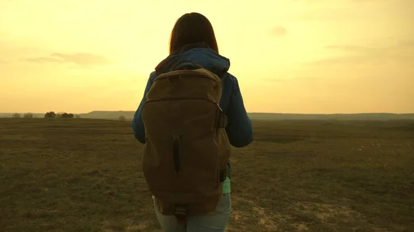 Ragazza che viaggia con uno zaino contro il cielo e il bagliore del sole. turista giovane donna va su un tramonto sulle montagne. desiderio di conoscenza del mondo. concetto di turismo sportivo . — Foto Stock