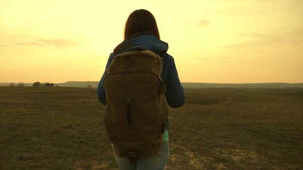 girl traveling with a backpack against the sky and the flare of the sun. tourist young woman goes on a sunset to the mountains. desire for knowledge of the world. sports tourism concept.