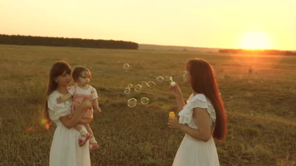 Mamma blåser tvål bubblor Happy Kids leende. Döttrar gläds och ler, bubblor flyger i parken vid solnedgången. Slow motion. Konceptet med en lycklig familj. barn, Syster och mamma spelar på Sunrise. — Stockvideo