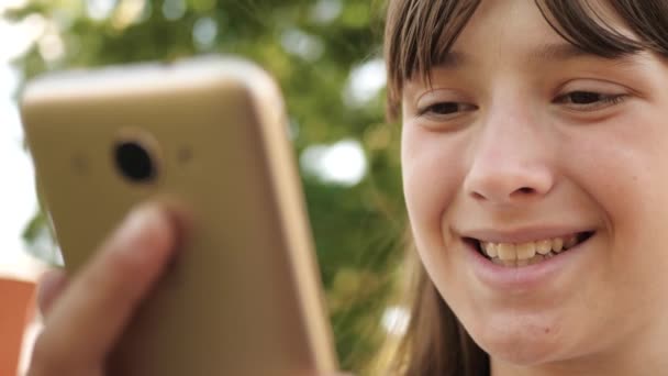 소녀는 지구상에서 온라인으로 채팅하고 있습니다. 클로즈업할 수 있습니다. 벤치에 공원에서 인터넷에서 페이지를 통해 플립 스마트 폰을 사용하여 행복한 소녀. — 비디오