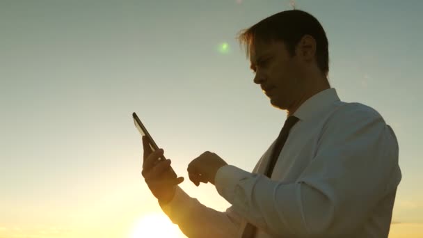 Businessman working on tablet at sunset in park. agronomist works with the tablet in field. farmer on plantation with smartphone. hands of man are driving their fingers over tablet. man checks email. — Stock Video