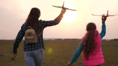 Mutlu kız kardeşler sahada gün batımında bir oyuncak uçak ile çalıştırın. Mutlu bir aile kavramı. çocuklar oyuncak uçak oynarlar. Kızlar uçmayı ve pilot olmayı hayal ler. Yavaş çekim