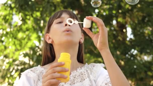 Gelukkig meisje mooi zeepbellen blazen in het park in de lente, zomer en glimlachen. Slow-motion. jong meisje reizen door de stad in het park. — Stockvideo
