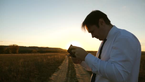 Hombre de negocios jugando juegos de tableta en el parque en los cálidos rayos de la puesta de sol. hombre jugando juegos en el teléfono inteligente. hombre feliz en camisa blanca y corbata juega en línea en la tableta . — Vídeos de Stock