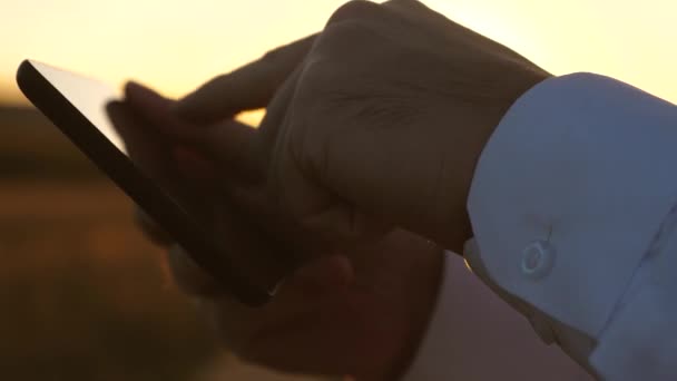 Hands of man are driving their fingers over tablet. man checks email. Businessman working on tablet at sunset in park. agronomist works with the tablet in the field. farmer on plantation with — Stock Video