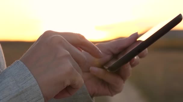 Dedos de niña pantalla táctil de la tableta, smartphone. Primer plano. Las manos femeninas sostienen una tableta y revisan los correos electrónicos en el parque al atardecer. niñas de la mano imprime un mensaje móvil en la pantalla del teléfono inteligente . — Vídeo de stock