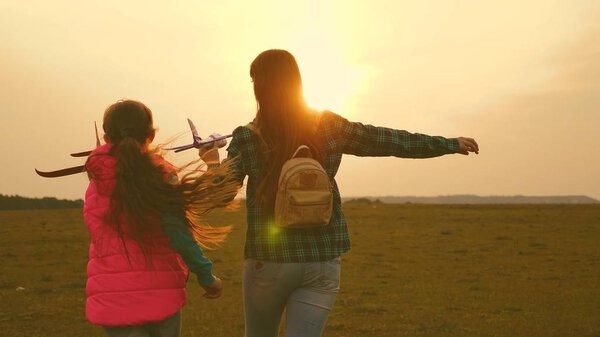 children play toy airplane. Happy girl sisters run with a toy plane at sunset on the field. The concept of a happy family. Girls dream of flying and becoming a pilot. Slow motion