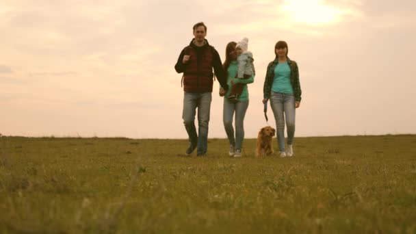 Familjen reser med hunden över fältet med ryggsäckar. Pappa, baby, Mamma, dotter och sällskapsdjur hund, turister. gemensamt arbete för en vänlig familj. Begreppet idrotts familj rekreation i naturen. — Stockvideo