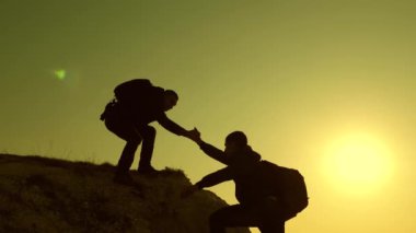 iş adamlarının takım çalışması. Dağcılar siluetler birbirlerine ellerini germek, tepenin üstüne tırmanma. gezginler kayaüzerinde birbiri ardına tırmanıyorlar. Bir işadamı takımı kazanacak..