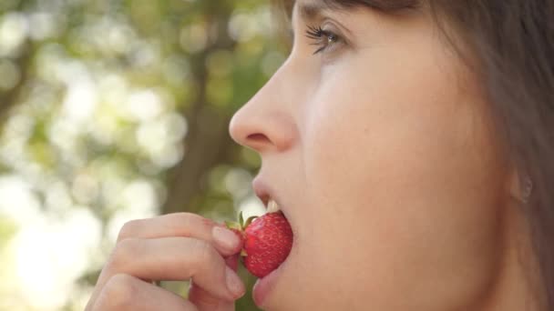 Menina feliz comendo morangos no verão no jardim. Deliciosa sobremesa de morango. menina bonita comer rugas de morango azedo e sorrindo. close-up. Dieta de vitamina e baga para mulheres . — Vídeo de Stock