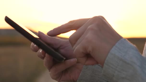 Fingers of girl touch screen of tablet, smartphone. close-up. Female hands are holding a tablet and checking emails in the park at sunset. girls hand prints a mobile message on the smartphone screen. — Stock Video