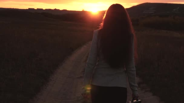 Uma mulher de negócios caminha ao longo de uma estrada rural com um tablet na mão, o sol miertsaet entre as pernas das mulheres. sexy mulher de negócios menina correndo no campo. sexy menina viaja no campo — Vídeo de Stock