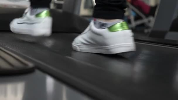 Benen van meisje in Sneakers op loopband close-up. versterking van de beenspieren door te lopen. wandelen in de fitnessruimte. cardio-belasting. meisje traint op een loopband. Fitness Club vrouw. gewichtsverlies in de sportschool. — Stockvideo