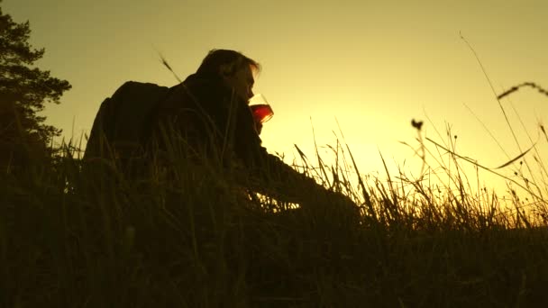 Turisten dricker hett te och tittar på solnedgången. Lonely Traveler sitter på toppen av en kulle dricka kaffe i termos. vila efter att ha nått målet. begreppet frihet och drömmar. världen utan gränser — Stockvideo