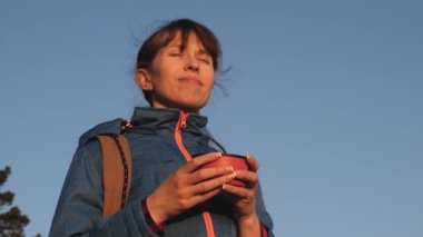 gezgin kadın sıcak çay içme ve mavi gökyüzüne karşı gün batımını izliyor. kız turist, termos bir bardak kahve içme tepenin üstünde duruyor. Goal ulaştıktan sonra Maceracı dinlenme. özgürlük kavramı.