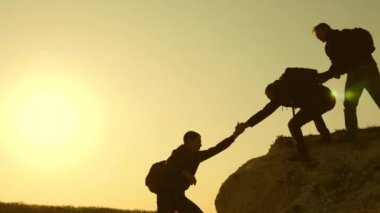 Dağcılar siluetler birbirlerine ellerini germek, tepenin üstüne tırmanma. gezginler kayaüzerinde birbiri ardına tırmanıyorlar. ortak iş. Yavaş çekim. iş adamlarının takım çalışması.