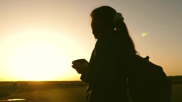 Silhouette kvinna Traveler, står på toppen av en kulle dricka kaffe i glas från termos. turist flickan dricker hett te och tittar på solen. Äventyrare vila efter att ha nått målet. frihets koncept. — Stockvideo