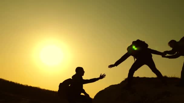 Teamwork der Geschäftsleute. Die Reisenden klettern nacheinander auf Felsen. Gemeinsame Sache. Zeitlupe. Bergsteiger Silhouetten strecken ihre Hände zueinander und klettern auf die Spitze des Hügels. — Stockvideo