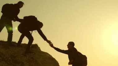 Dağcılar siluetler ellerini birbirlerine uzatır ve tepenin tepesine çıkarlar. gezginler kayaüzerinde birbiri ardına tırmanıyorlar. iş adamlarının takım çalışması. Bir grup işadamı.