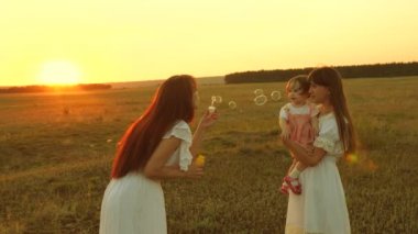 Kızlar sevinç ve gülümseme, kabarcıklar gün batımı parkta uçmak. Yavaş hareket. Mutlu anne çocuklar sabun kabarcıklar üfleme ile oynuyor. mutlu bir aile kavramı. Çocuk, kız kardeşi ve anne gündoğumu oyun.