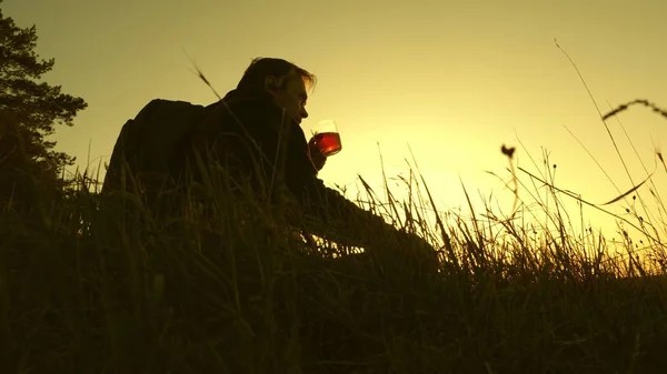 Турист пьет горячий чай и наблюдает закат. одинокий путешественник, сидящий на вершине холма и пьющий кофе в термосе. отдых после достижения цели. концепция свободы и мечты. мир без границ — стоковое фото