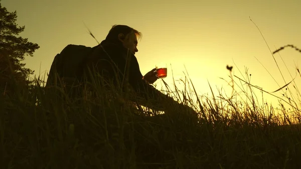 Bevande turistiche tè caldo e guarda il tramonto. Viaggiatore solitario seduto sulla cima di una collina a bere caffè in thermos. riposo dopo aver raggiunto l'obiettivo. concetto di libertà e sogni. mondo senza frontiere — Foto Stock