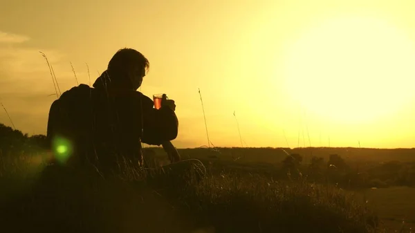 Viajero solitario sentado en la cima de una colina bebiendo café en termos. turista bebe té caliente y observa atardecer. descansar después de alcanzar la meta. concepto de libertad y sueños. mundo sin fronteras — Foto de Stock