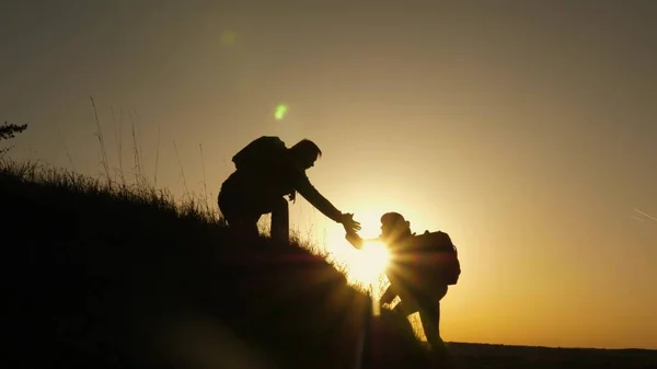 Viaggiatore uomo tende la mano ad una ragazza che sale in cima ad una collina. i viaggiatori scalano la scogliera tenendosi per mano. lavoro di squadra di uomini d'affari. Famiglia felice in vacanza. i turisti si abbracciano in cima alla montagna — Foto Stock