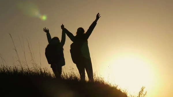 Mamma och dotter på semester resor och dans på berget. Kvinna med upphöjda händer på toppen av berget tittar på solnedgången. Vandrare flicka höja hennes hand upp, fira seger och njuta av landskap. — Stockfoto