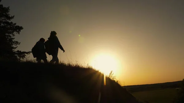 Mutter und Tochter reisen in den Urlaub. Frau mit erhobenen Händen auf einem Berg und Blick auf den Sonnenuntergang. Wandermädchen hebt die Hand, feiert den Sieg und genießt die schöne Landschaft und die Natur. — Stockfoto