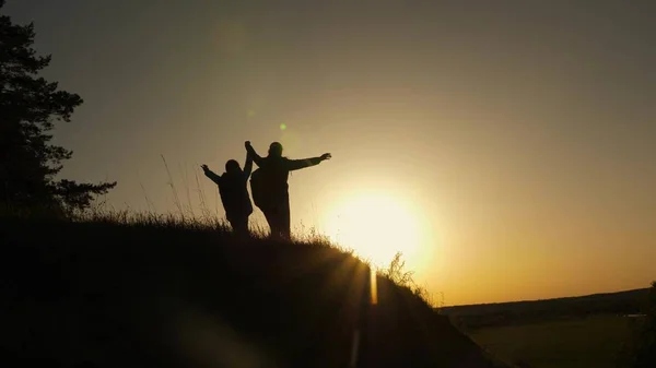 Сім'я мама і дочка подорожі відпустку. Жінка з піднятими руками на вершині гори дивиться на захід сонця. Мандрівні дівчата піднімають руку вгору, святкуючи перемогу і насолоджуючись красивими пейзажами і природою. — стокове фото