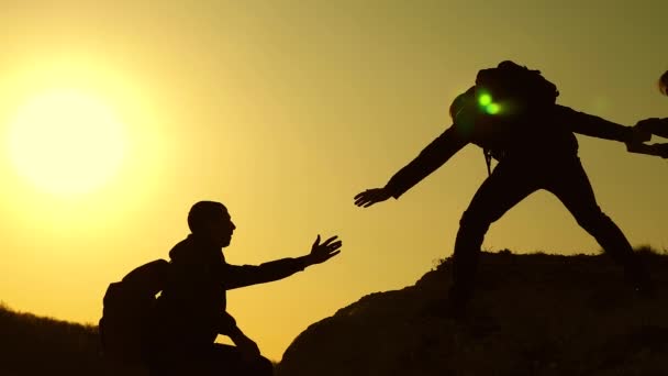 Collaborazione arrampicatori viaggiatori al tramonto. Silhouette di uomini che salgono in cima alla montagna. I viaggiatori si arrampicano uno ad uno sulle rocce. Affari congiunti. Rallentatore — Video Stock