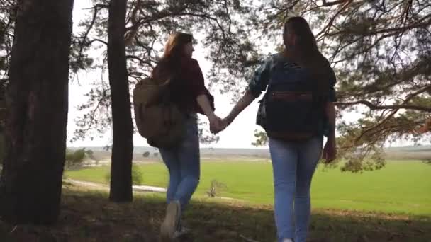 Vrouwen toeristen gaan door het bos. Sexy vrouwelijke reizigers met rugzakken rechttrekken hun armen aan de zijkant, genietend van vrijheid. Vriendinnen houden van handen en lachen. Avonturen in de campagne. Teamwork. — Stockvideo