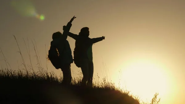 Hiker Girl Levantando la mano, celebrando la victoria y disfrutando del paisaje. mamá y su hija de vacaciones viajando y bailando en la montaña. Mujer con las manos levantadas en la cima de la montaña mirando el atardecer . — Foto de Stock