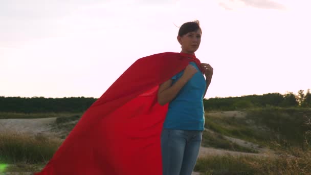 Superhero dziewczyna w czerwonym płaszczu przeciwdeszczowego macha na wiatr uśmiechy. Młoda dziewczyna marzy o zostaniu superbohaterem. Dziewczyna idzie w czerwonym płaszczu z ekspresją marzeń. Zwolnionym. — Wideo stockowe