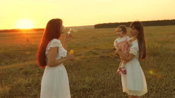 Le figlie gioiscono e sorridono, le bolle volano nel parco al tramonto. Al rallentatore. Madre felice che gioca con i bambini soffiando bolle di sapone. concetto di una famiglia felice. bambino, sorella e madre giocano all'alba . — Video Stock