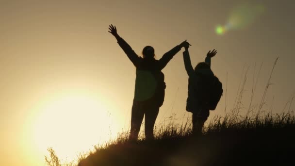 休暇旅行や山で踊るママと娘。夕焼けを見て山の頂上に手を上げた女性。ハイカーガールは手を上げ、勝利を祝い、景色を楽しむ. — ストック動画