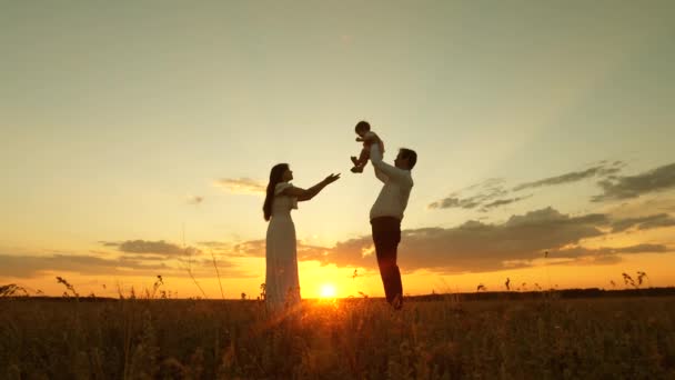 Papá tiene en sus manos a una pequeña y feliz hija y se la da a su madre. hija juega con mamá y papá al sol. concepto de familia feliz y la infancia. familia feliz descansando en el parque en los rayos de la puesta del sol — Vídeos de Stock