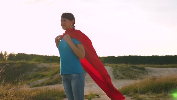 Hermosa chica sueña con convertirse en un superhéroe. sexy chica superhéroe de pie en el campo en una capa roja, capa revoloteando en el viento. En cámara lenta. chica joven en una expresión de sueño capa roja — Vídeos de Stock