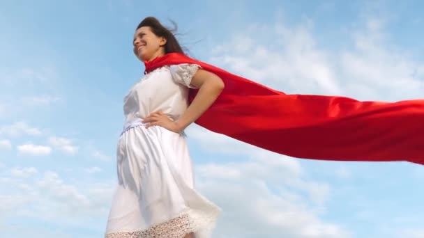 Schöne Mädchen träumt davon, ein Superheld zu werden. sexy Superheldenmädchen steht auf dem Feld in einem roten Mantel, Mantel flattert im Wind. Zeitlupe. junges Mädchen in einem roten Umhang Traumausdruck — Stockvideo